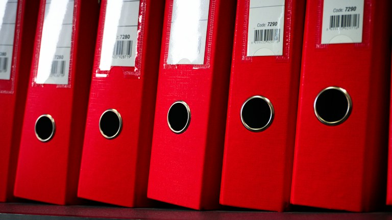 Red file folders are neatly arranged on a shelf