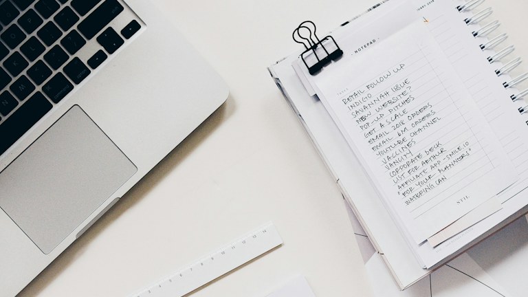 Paper notes and pen beside a laptop