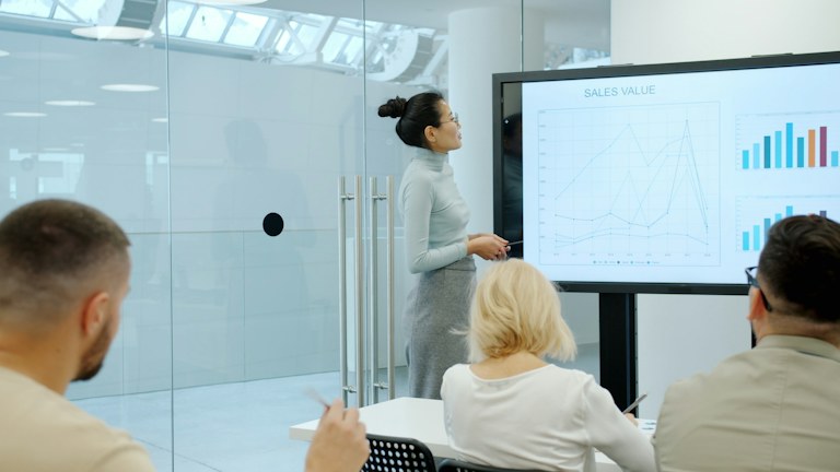 Woman presents charts on a screen to colleagues