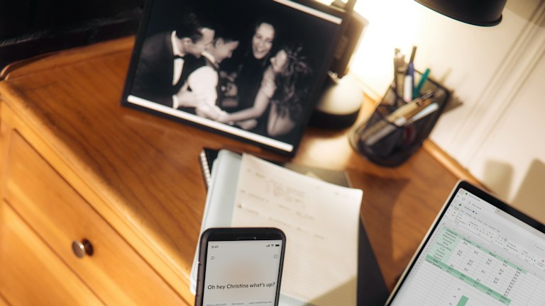 Person holding phone near laptop and tablet on desk